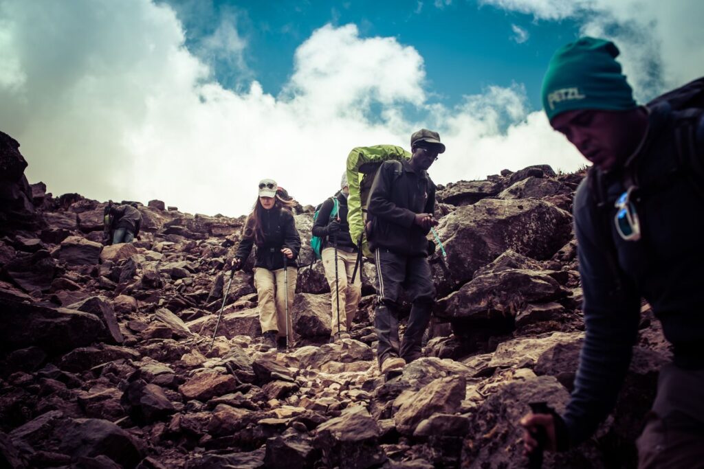A diverse group of hikers navigating a rocky mountain trail under a bright sky.